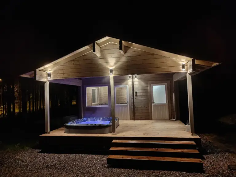Saunamökki 25, jossa on ulkoporeallas, valaistuna yön pimeydessä.