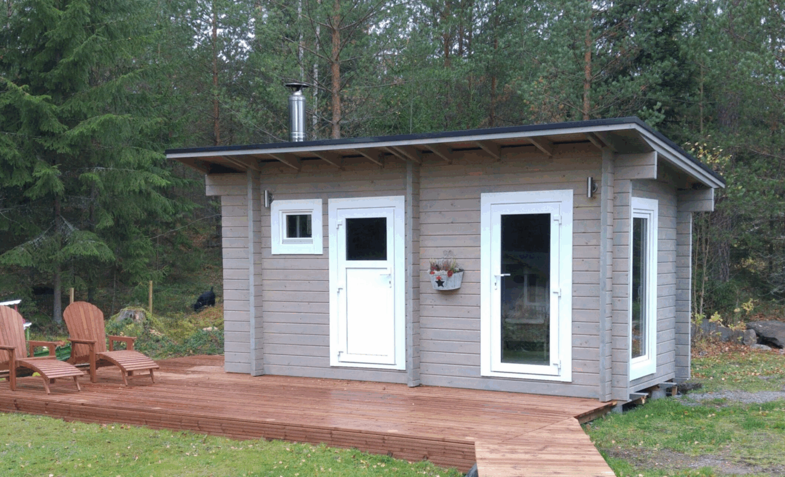 Pieni valmismökki metsässä terassin päällä